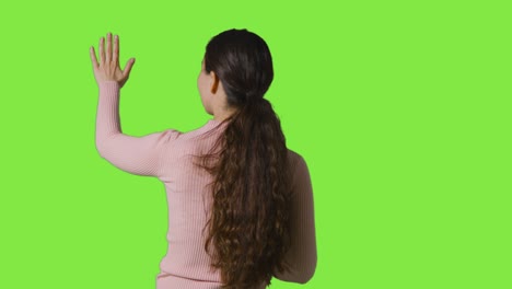 Rear-View-Studio-Shot-Of-Woman-Looking-And-Touching-Against-Green-Screen-In-VR-Environment-1